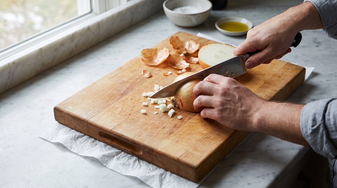 Hands slicing onion on a wooden board with a damp towel underneath to stop the cutting board sliding