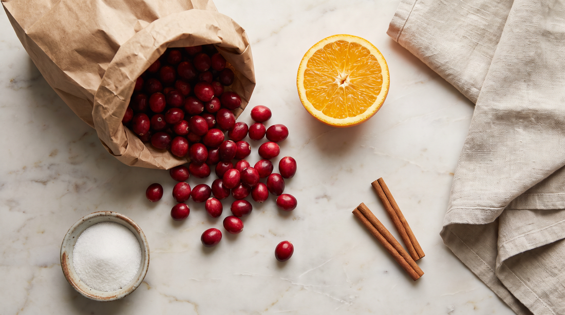 Fresh cranberries, orange halves and sugar laid out for homemade cranberry sauce in a titanium pot
