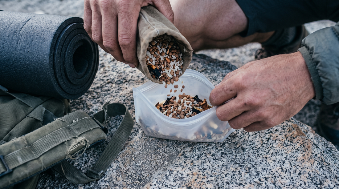 Hands portioning dried rice and lentils for backpacking cookware meals on a granite slab