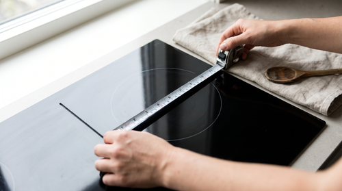 Hands measuring a glass cooktop ring with a tape measure when matching pan size to hob ring