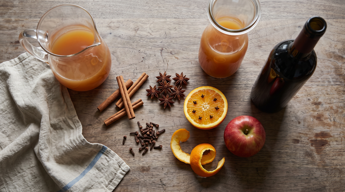 Cinnamon, cloves, star anise, orange peel and cider laid out for mulled wine in a titanium pot
