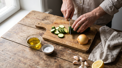 Hands slicing zucchini on a small apartment counter, prep space for portable electric hotplate cooking