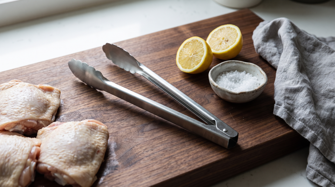 Stainless vs silicone tipped tongs comparison: metal tongs on a board with raw chicken and lemon